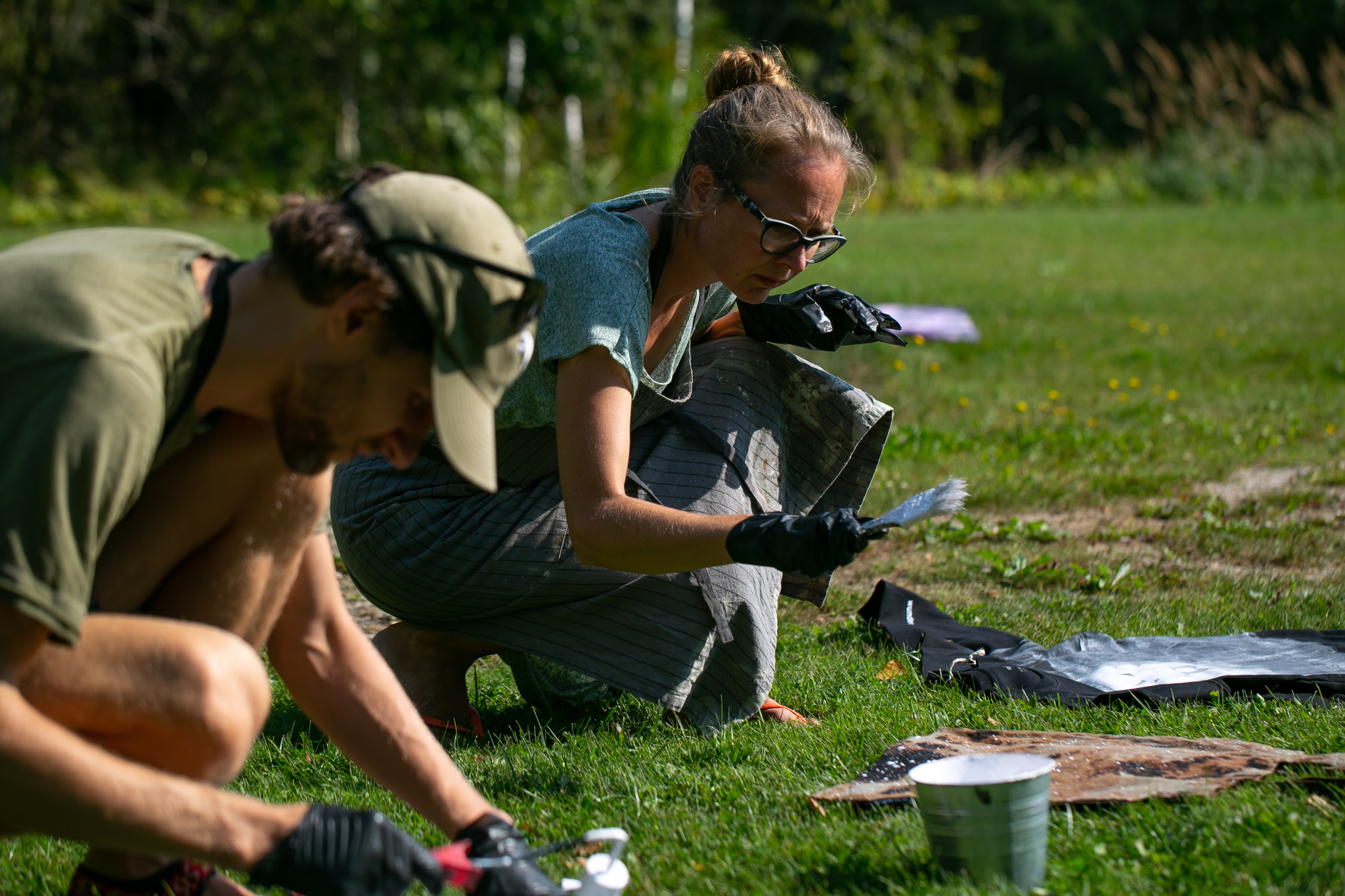 Outside workshop where two people are sitting on grass and painting clothes.
