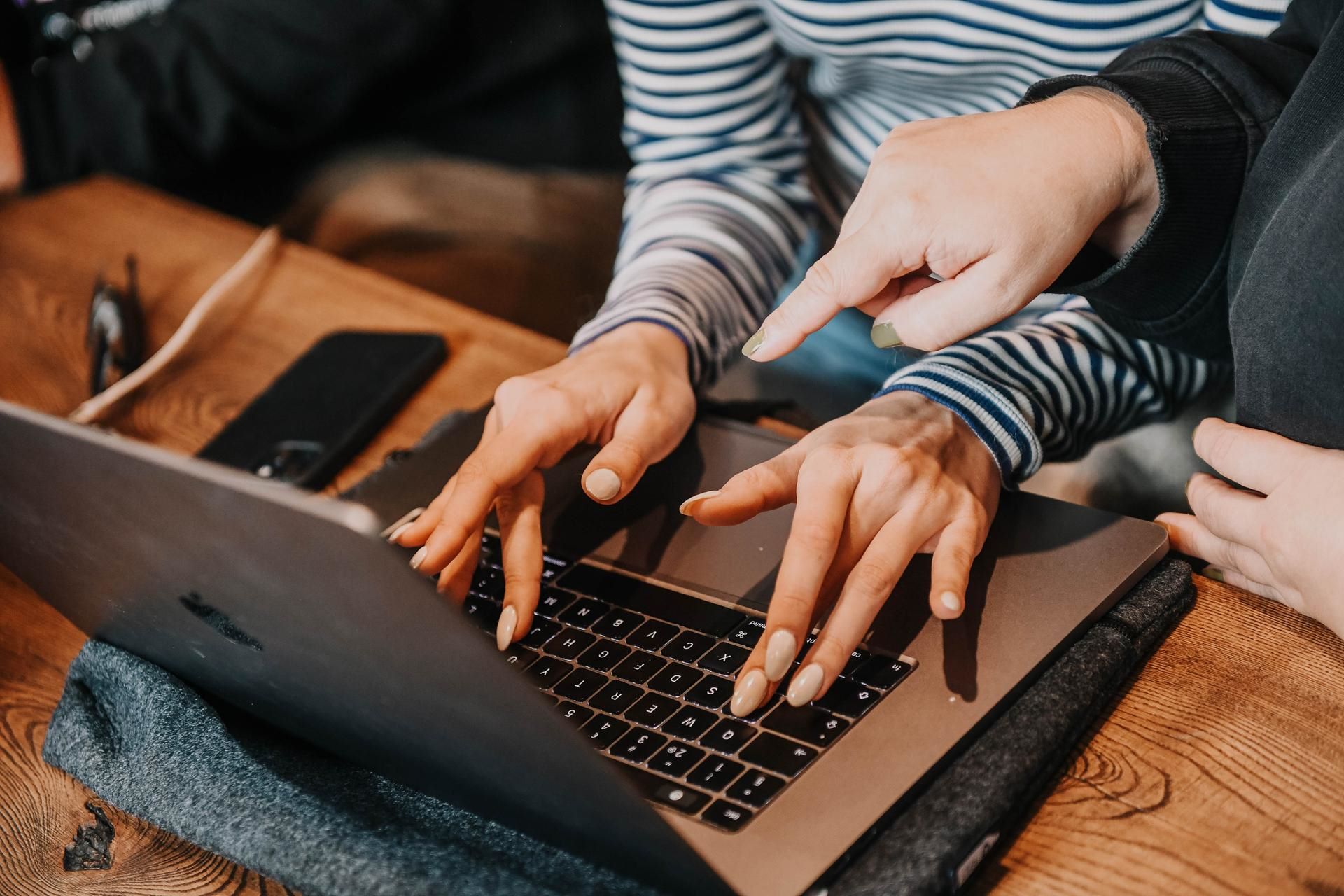 Person typing on laptop, other pointing at screen.