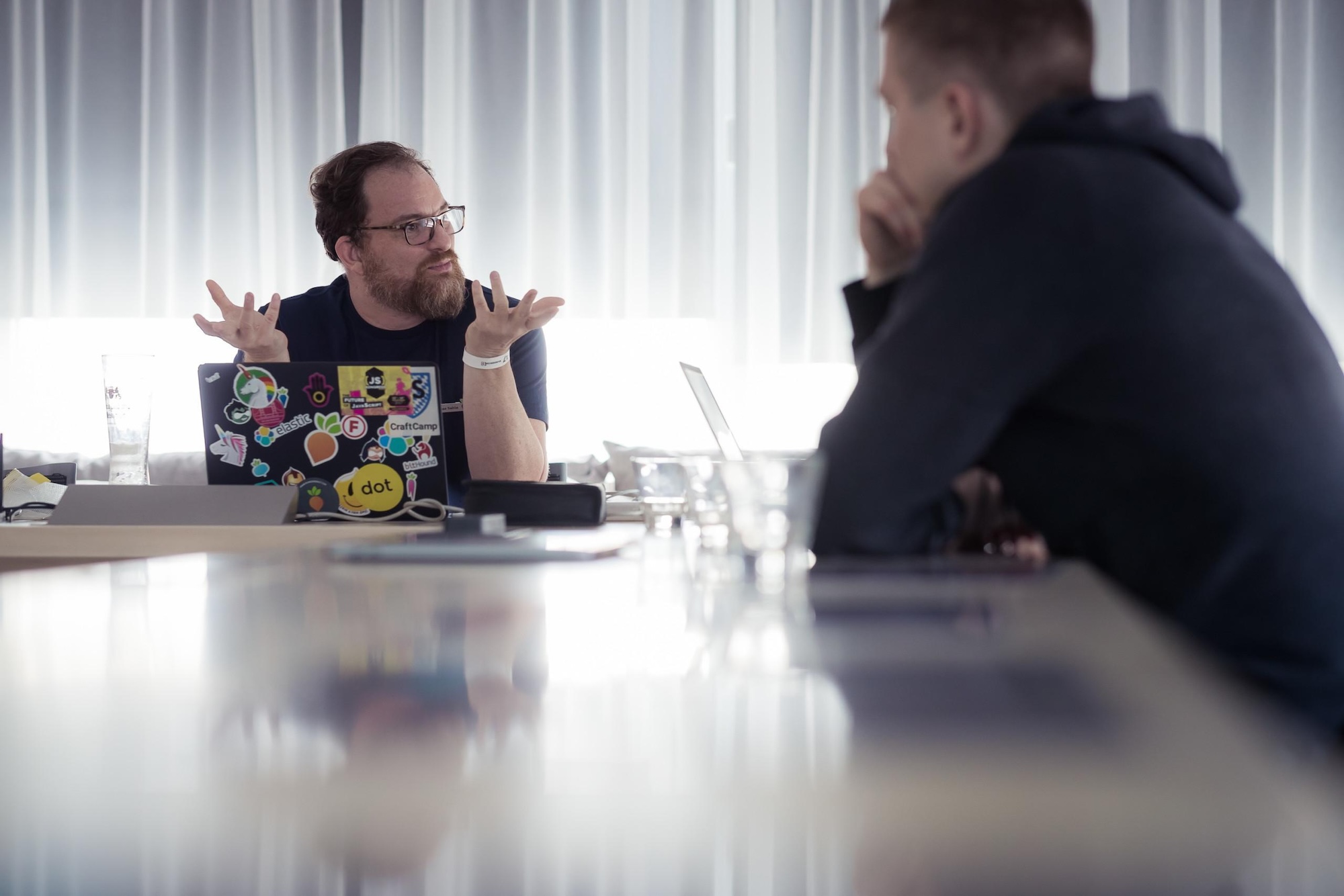 Two people sitting at the table laptops open and conversing.