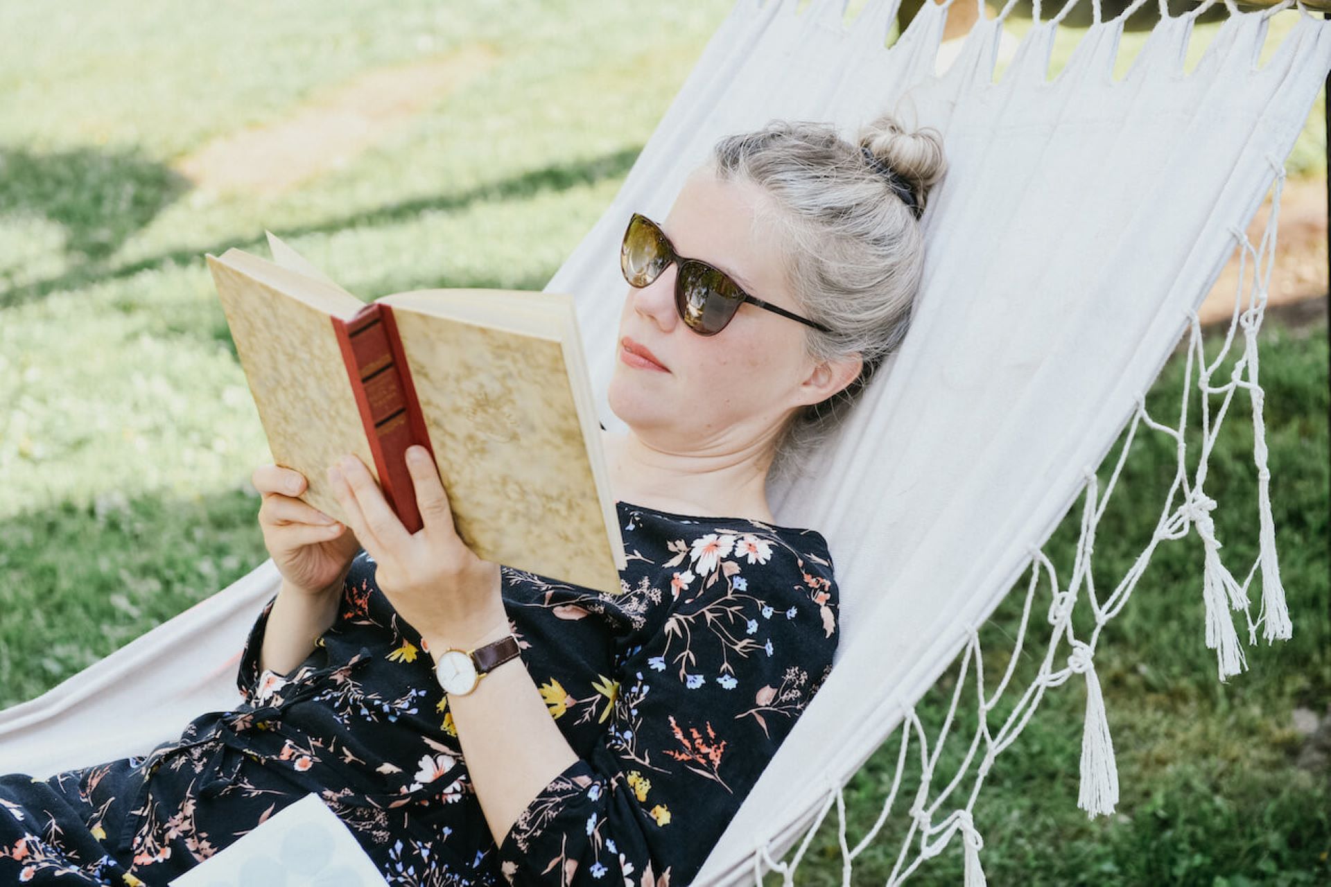 Summer woman lies in a white hammock reading a book.