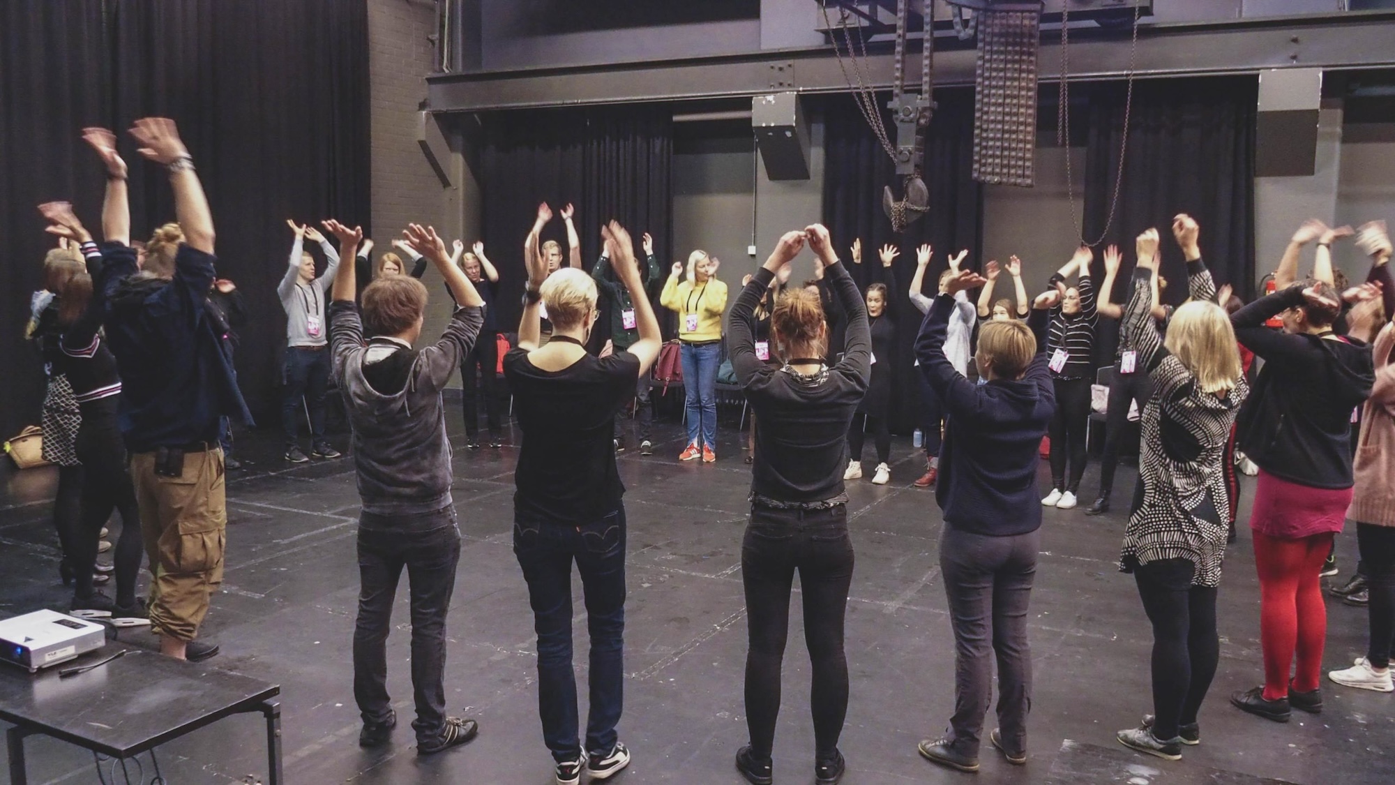 People standing in circle formation with their hands up in the Joyhacking event.