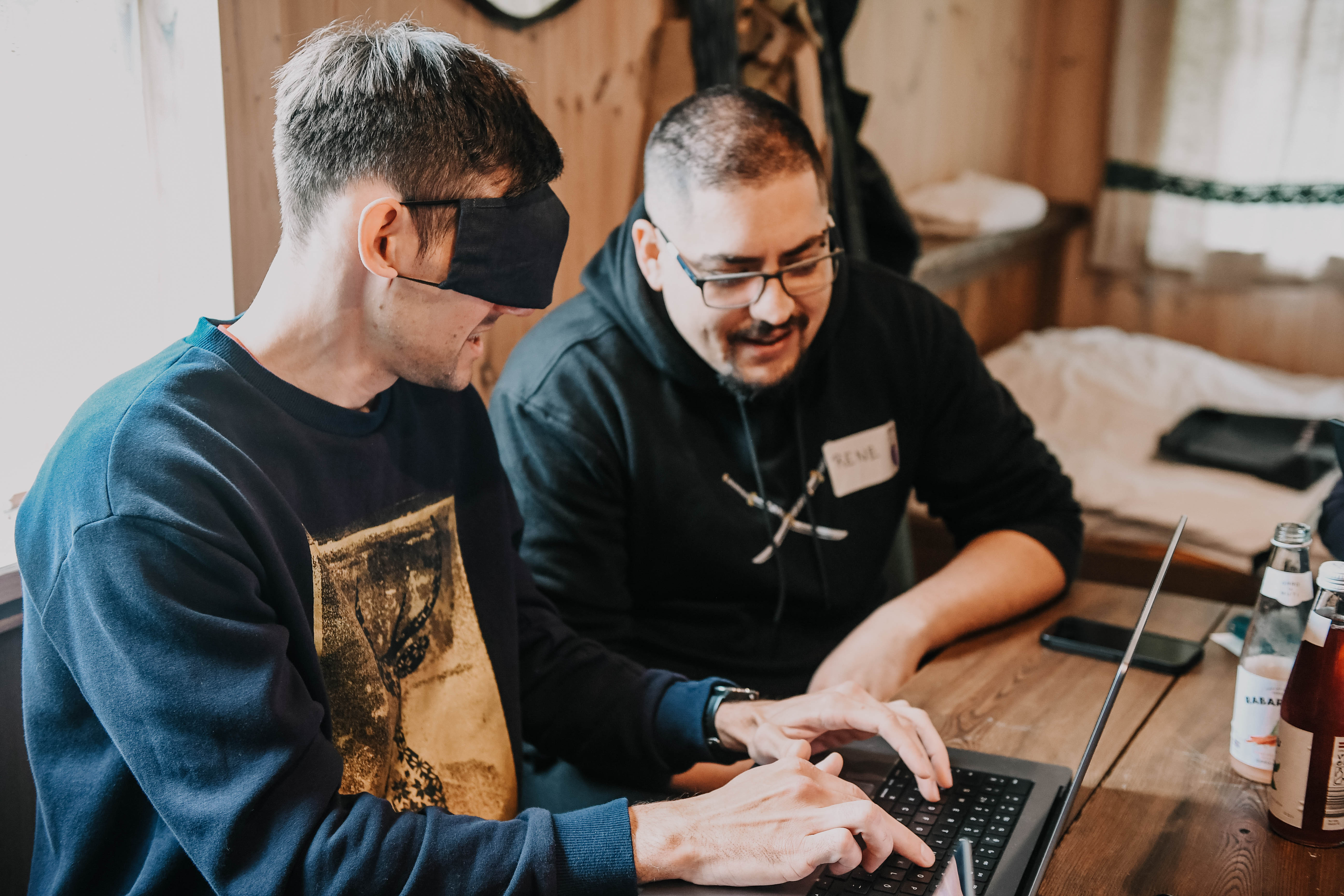 A person showing a blindfolded person how to operate a keyboard with speech